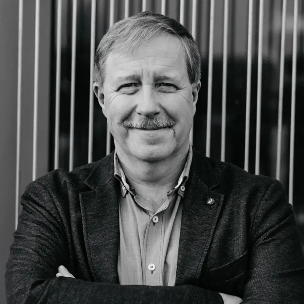 Erfahrener Bauleiter mit Schnurrbart, verschränkten Armen und Hemd vor moderner Fassade – STUDIO S Architekten Bocholt