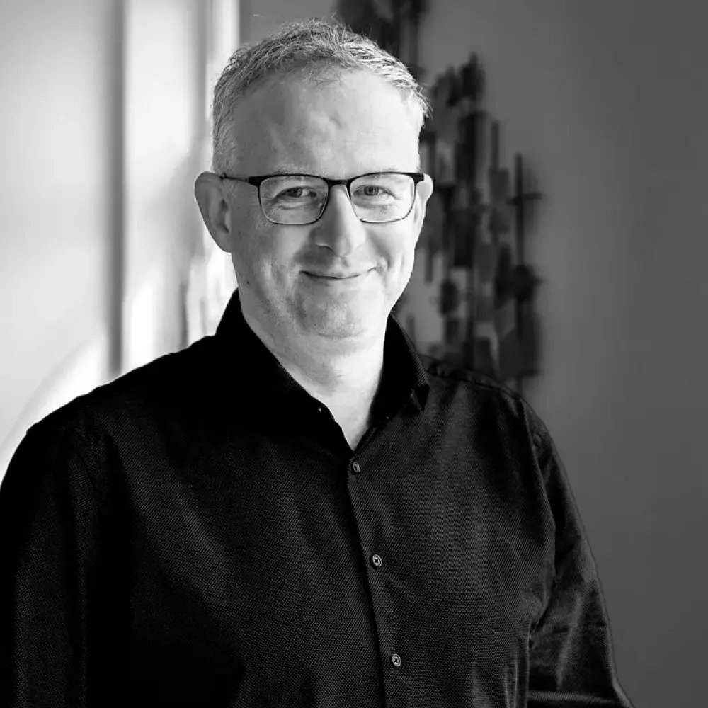 Porträt eines erfahrenen Architekten mit Brille, freundlich lächelnd im Büro von STUDIO S Architekten