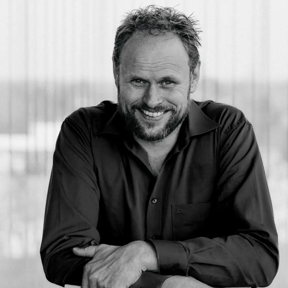 Porträt eines Mannes mit Bart in dunklem Hemd, der lächelnd in die Kamera blickt – entspannte und zugleich selbstbewusste Ausstrahlung.